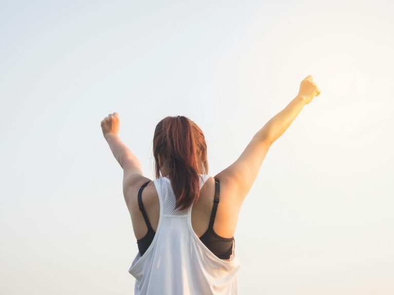 Selbstbewusst durch Kung Fu Eine Person mit erhobenen Armen blickt in den Himmel, Sonne scheint im Hintergrund.